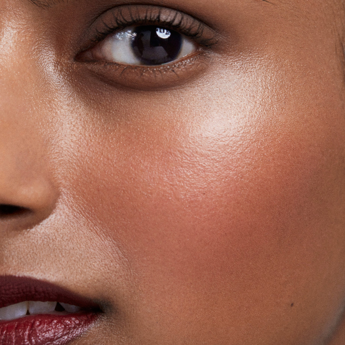 Close up of a person with a medium skin tone’s cheek and eye tone wearing cream blush