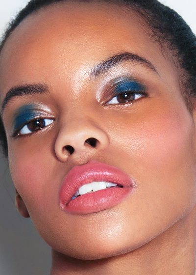 Close-up of a model's face showcasing makeup, featuring vibrant blue eyeshadow on the eyes and a soft pink lipstick on the lips.